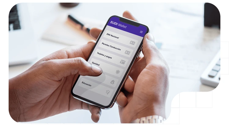 Primer plano de unas manos sosteniendo un teléfono móvil que muestra la pantalla principal de la aplicación EUDI Wallet.