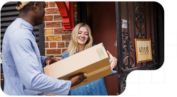 Persona repartiendo un paquete grande a una mujer sonriente en la puerta de su casa