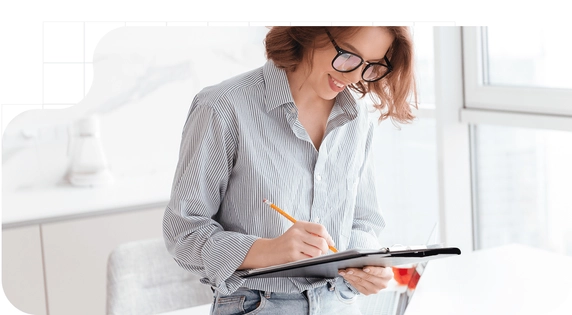 Woman wearing glasses filling out a form related to a recognized electronic signature on a clipboard, in a bright workspace next to a window.