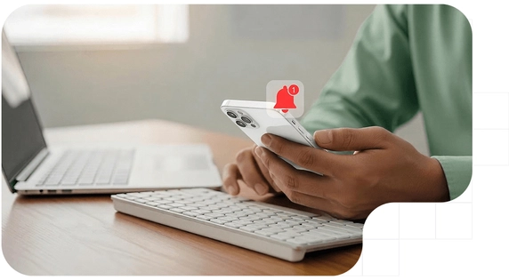 Persona recibiendo una notificación fehaciente en su móvil mientras trabaja con el ordenador.