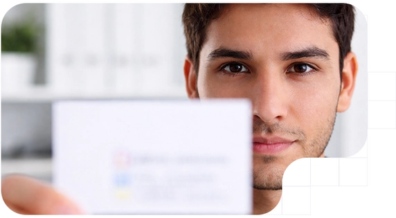 Close-up of a young man looking at the camera while holding an ID card in close-up, in a bright, modern indoor setting.