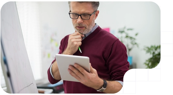 Profesional analizando datos en una tablet frente a una pizarra.